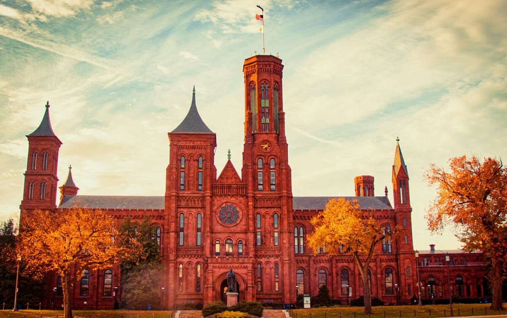 Historic red brick building with towers and a central clock under a blue sky with wispy clouds, featured in the Family-Friendly Guide to the Smithsonian.