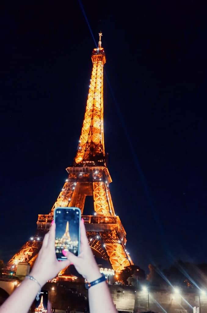 A person taking a photo of the eiffel tower at night.